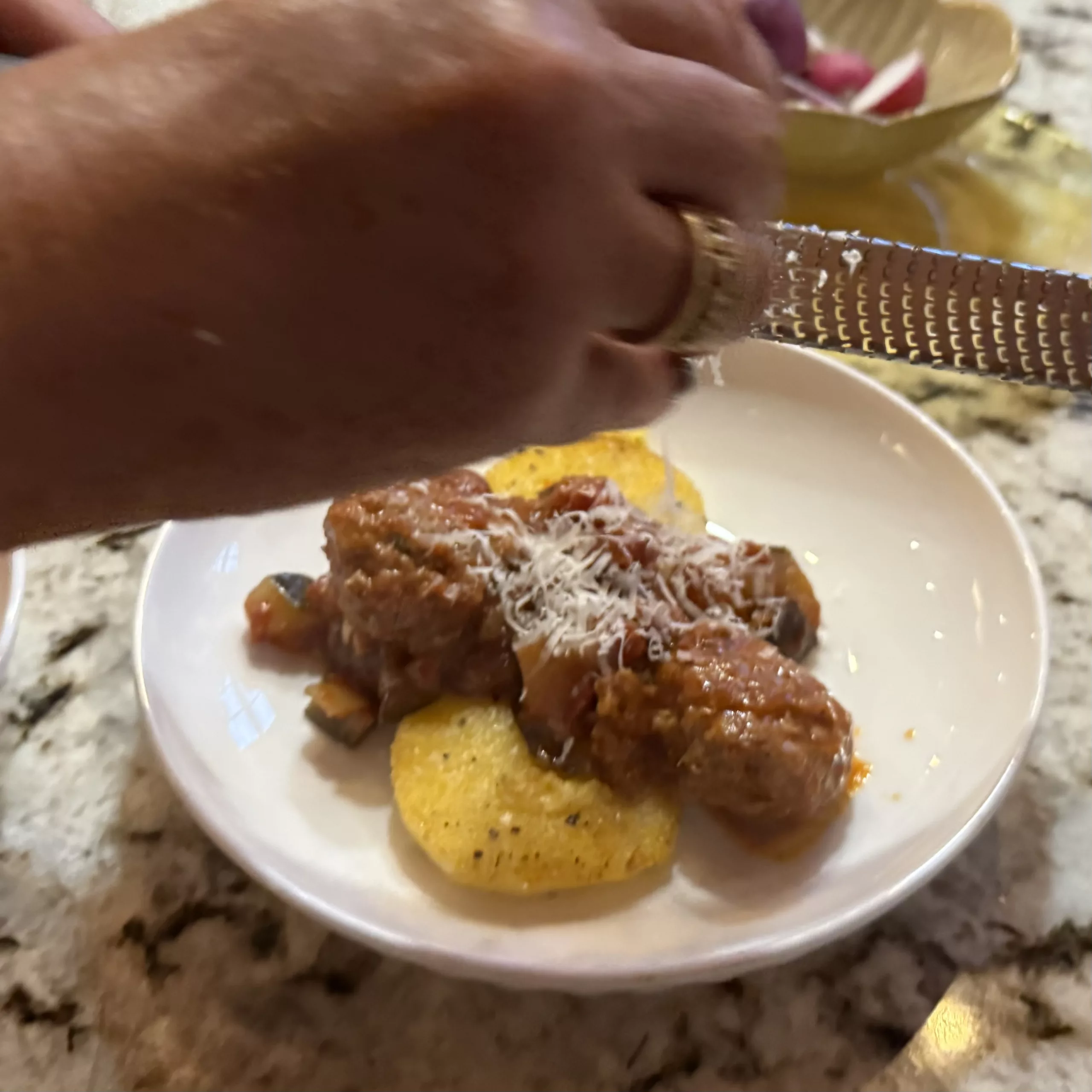 Shredding Parmesan over meatballs