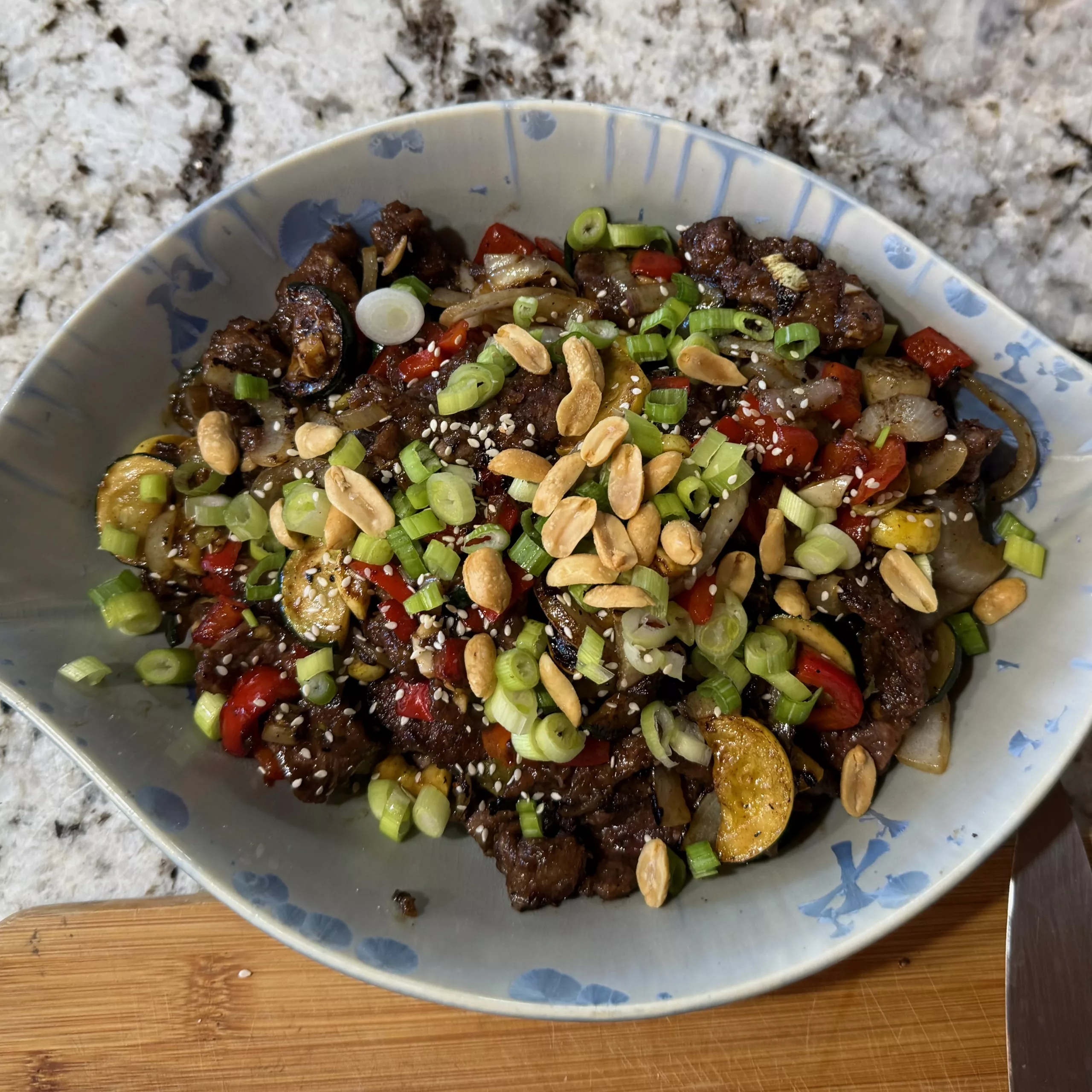 Plated stir fry topped with scallions, peanuts, and sesame seeds